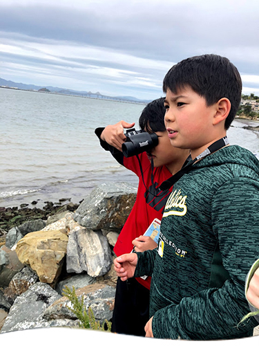 Two boys with binoculars looking at the water